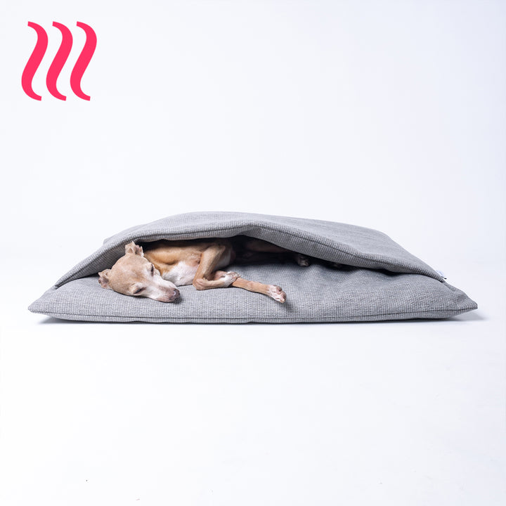 Italian Greyhound dog sleeping in a luxury sleeping bag style dog burrow bag by Charley Chau in a grey woven upholstery fabric on a white background.