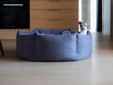 A dog inside a dark gray donut dog bed with deep cosy sides in a modern kitchen with wooden floor