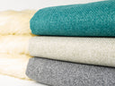 Three spare dog bed covers in jade, beige and grey, folded in a stack on a white background