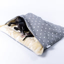 A black dog sleeping in a dog bed with cover - a Charley Chau luxury dog burrow bag in a pale grey polka dot fabric with a cream faux-fur lining on a white backdrop.