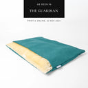A sleeping bag style dog bed by designers Charley Chau, The Dog Burrow Bag, in a jade green upholstery fabric with cream plush lining on a white backdrop with an "As seen in The Guardian" featured in the press badge.