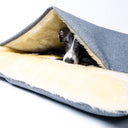 Close up of a dog sleeping very cosy inside a grey luxury dog burrow bag, a snuggle sack type of dog bed, with a cosy cream Faux-Fur lining on a white backdrop.