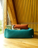 Dog lying on a jade green bolster pet bed with colorful pillows in a modern indoor setting.