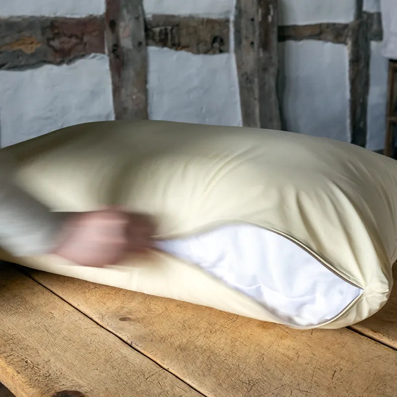 Cream colur anti-microbial dog bed mattress protector beng unzipped with a white dog bed mattress inside on a wooden table.