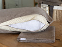 A luxury dog bed mattress with the uoter cover zip undone to show a cream waterproof bed linert and internal mattress, with a folded spare bed cover on a wooden table. 