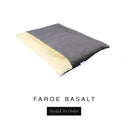 A luxurious Dog Burrow Bag, a sleeping bag style dog bed or snuggle sack style dog bed, with an outer cover in dark grey woven wool texture upholstery fabric Faroe with a plush, cream faux-fur lining, and a badge with the colour name Basalt on a white background.