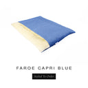 A luxurious Dog Burrow Bag, a sleeping bag style dog bed or snuggle sack style dog bed, with an outer cover in bright blue woven wool texture upholstery fabric Faroe with a plush, cream faux-fur lining, and a badge with the colour name Capri Blue on a white background.