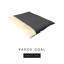 A luxurious Dog Burrow Bag, a sleeping bag style dog bed or snuggle sack style dog bed, with an outer cover in charcoal black woven wool texture upholstery fabric Faroe with a plush, cream faux-fur lining, and a badge with the colour name Coal on a white background.