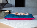 A dog keeping cool sleeping stretched out on a luxury dog bed mattress in teal and pink velvet, on a grey rug in a home setting.