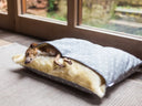 Dog lying inside a sleping bag style dog bed, the original Charley Chau Dog Snuggle Bed, with a grey polka dot cotton outer cover and fluffy cream lingin on the inside in a home setting in front of windows.
