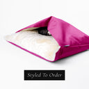 Fuchsia Pink Velvet cave bed style Snuggle Dog Bed by designers Cahrley Chau with a cream, plush lining and a dog sleeping inside the bed on a white background.