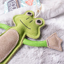 Close up of agreen and brown frog-shaped dog toy placed on a fluffy silver-grey faux-fur dog blankets.