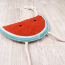 Eco-friendly dog toy made from suede, shaped like a watermelon slice, with rope arms and legs, on a wooden floor