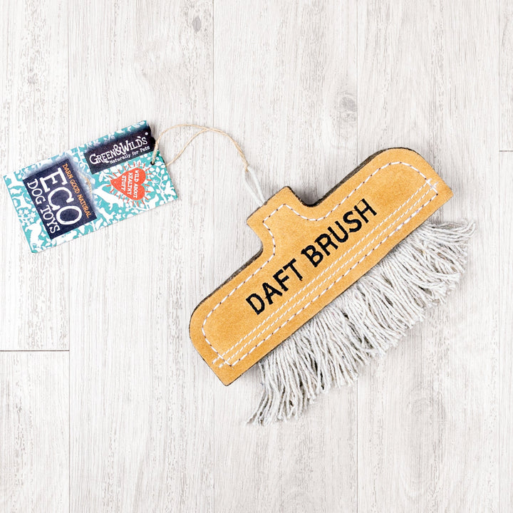 An eco-friendly dog toy in the shape of a cleaning brush in a tan coloured suede with grey string on a pale oak floor. 