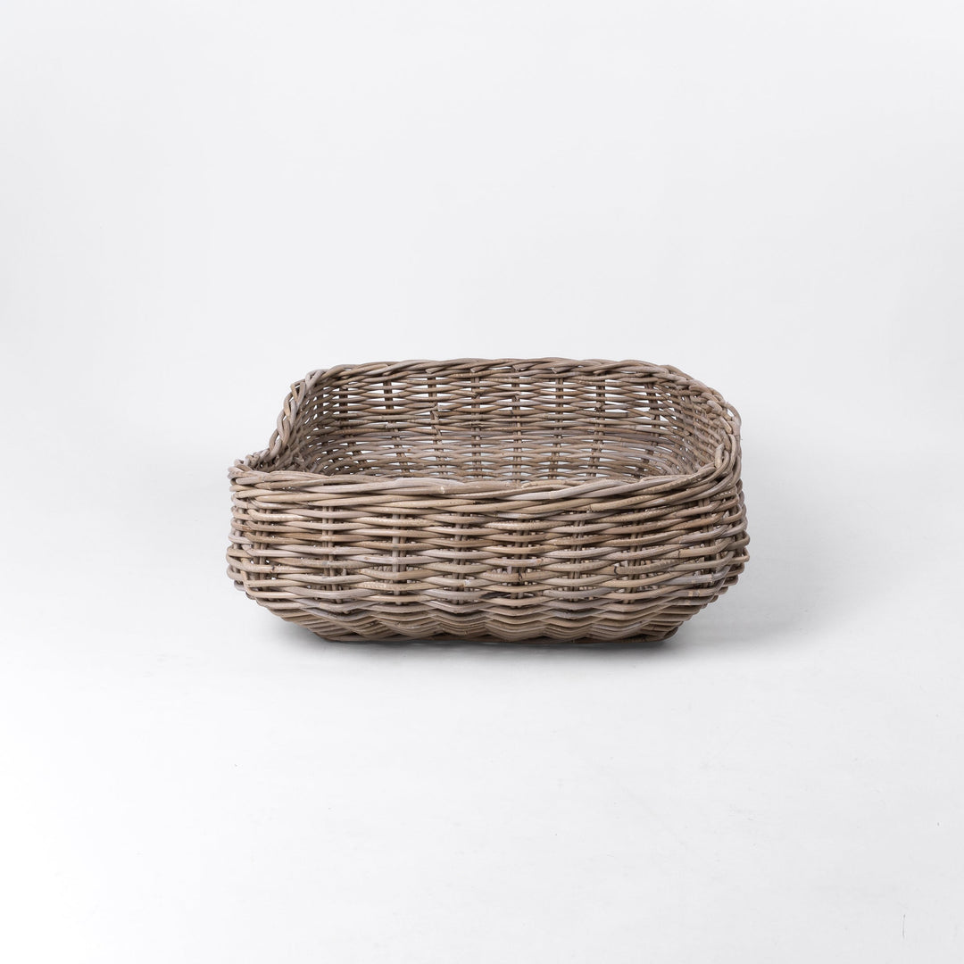 A classic wicker dog basket - a grewash rattan dog basket - woven with natural rattan canes, on a white background, viewed from the side.