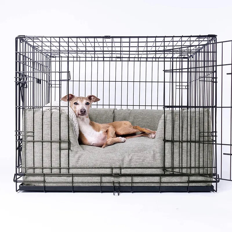 Dog lying on a grey, high-sided luxury dog bed inside a dog crate with a white background.
