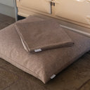 Folded spare dog bed cover placed on top of a luxury dog bed mattress on a stone floor in a home setting.