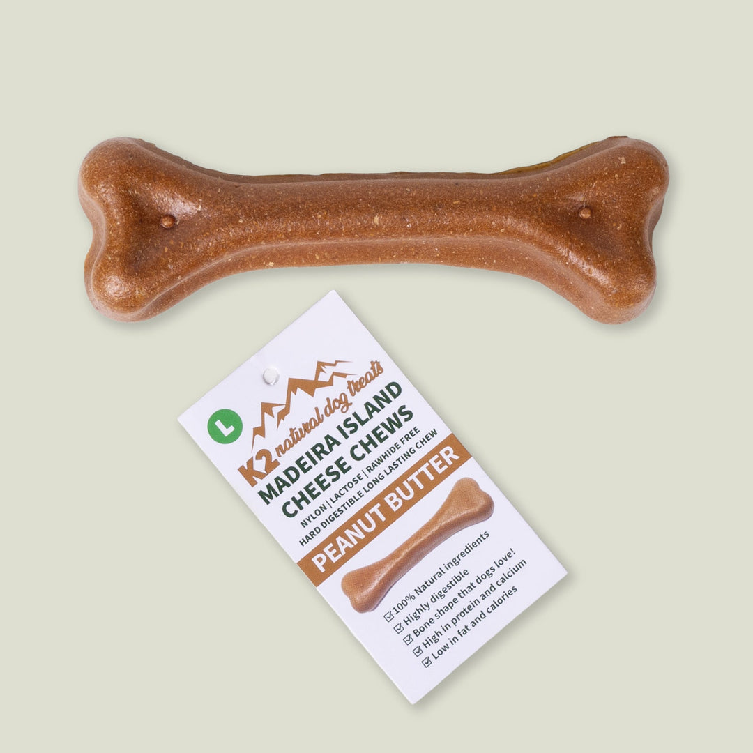 A brown, bone-shaped, natural dog chew treat made from Madeira Cheese and Peanut Butter, with it's product label, on a pale sage green background.