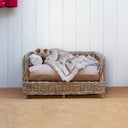 A beautiful wicker dog bed, the Raised Rattan Dog Bed, with luxury dog bed mattress and faux-fur dog blanket in a hallway.