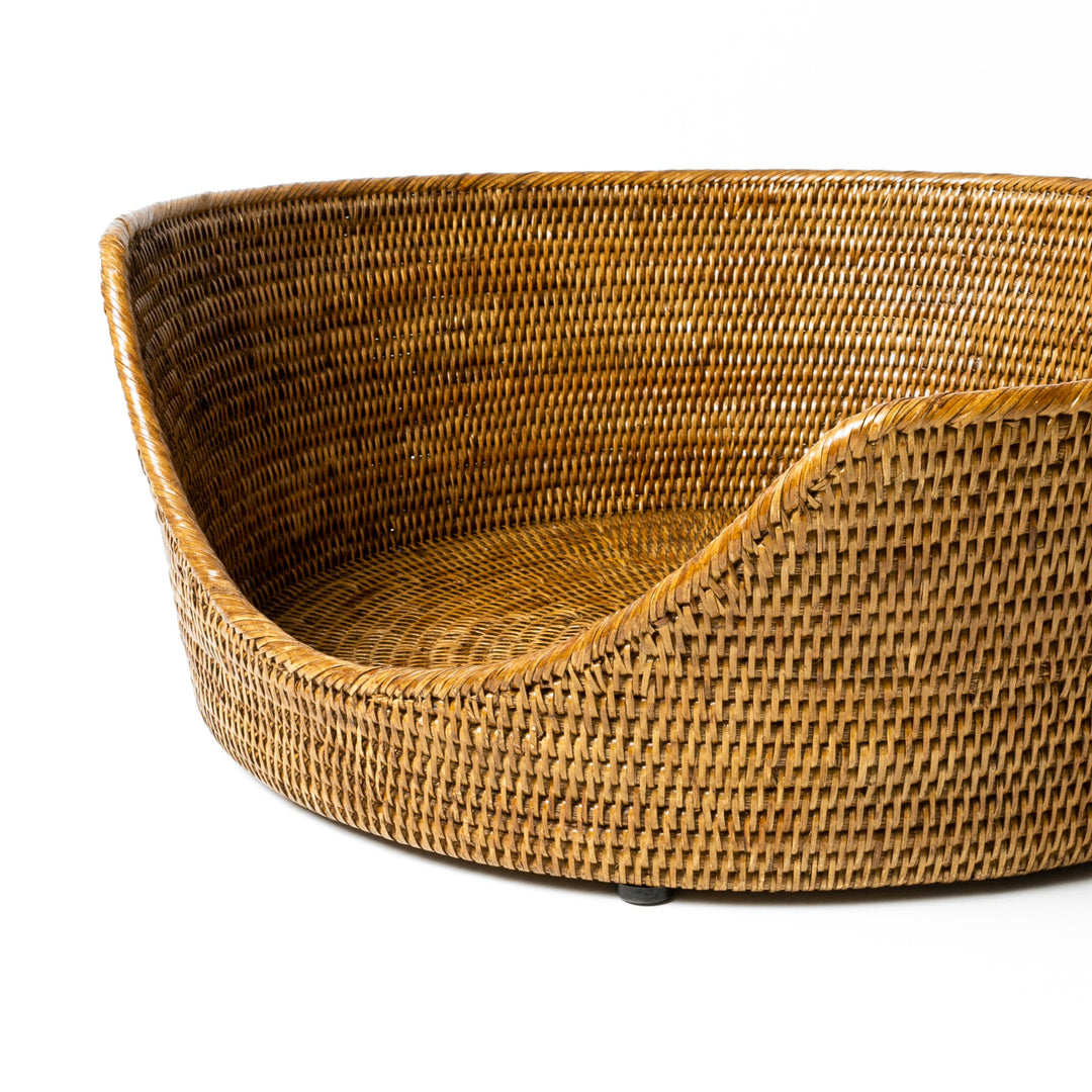 An close up detail shot of the front of a  tan beige coloured round rattan dog basket on a white background.