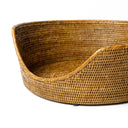 An close up detail shot of the front of a  tan beige coloured round rattan dog basket on a white background.