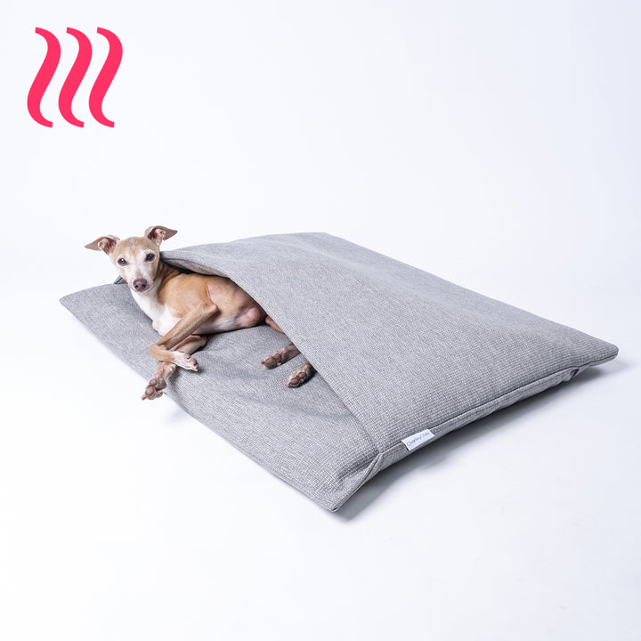 Italian Greyhound dog lying in a luxury sleeping bag style dog burrow bag by Charley Chau in a grey woven upholstery fabric with the Charley Chau brand label visible, on a white background.