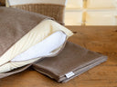 Close up of a machine washable Charley Chau luxury dog bed mattress in beige, with the zip open revealing a waterproof mattress protector and white internal luxury mattress, placed on a table with a folded spare dog bed cover.