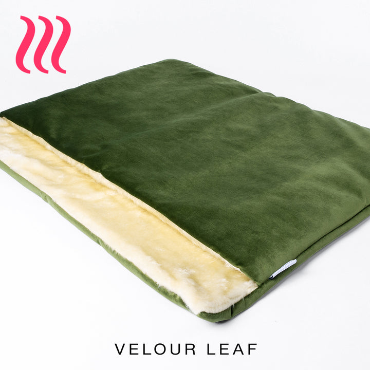 Luxury sleeping bag stlye dog bed outer cover in leaf green colour velvet with a cream faux-fur lining on a white background.