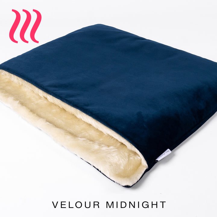 Luxury sleeping bag stlye dog bed outer cover in dark blue colour velvet with a cream faux-fur lining on a white background.
