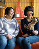 Two women, Jenny & Christine Chau, co-founders of luxury dog bedding company Charley Chau, sitting on sofa holding an Italian Greyhound dog.