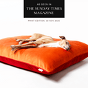 Dog lying on an orange and red velvet luxury dog bed mattress with 'As seen in The Sunday Times Magazine' press feature badge above.