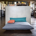 Grey luxury dog bed mattress with two small mini-bolster pad cushions on top in jade green and orange, in a home setting with a wooden floor. 