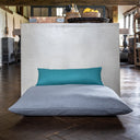 Grey luxury dog bed mattress with a small jade green mini-bolster pad cushion on top in a home setting with a wooden floor. 