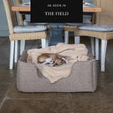 Beige luxury high-side dog bed, the Deeply Dishy Dog Bed by designers Charley Chau, with an Italian Greyhound dog sleeping on a teddy beige sherpa dog blanket in a home setting with an 'As seen in The Field' press feature badge above.