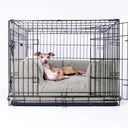 Black wire dog crate with a luxurious grey deep-sided dog bed inside it and an Italian Greyhound dog lying in the bed looking very comfortable on a white backdrop.