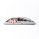 Italian Greyhound Dog looking comfortable and calm lying inside a luxury dog burrow bag, a snuggle sack style dog bed with a built in cover, in a woven grey upholstery fabric on a white background