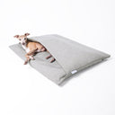 Italian Greyhound Dog lying inside a luxury dog burrow bag, a sleeping bag style dog bed with a built in cover, in a woven grey upholstery fabric on a white background
