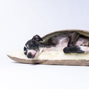 Close up of a black dog sleeping covered up in a snuggle sack style Dog Burrow Bag with a beige woven upholstery fabric outer cover and plush cream faux-fur lining.