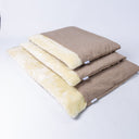 A stack of three luxury dog burrow bags. a sleeping bag style dog bed,  in three different sizes, all in a beige woven upholstery fabric with cream faux-fur lining on a white backdrop.