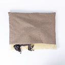 A black dog sleeping covered up in a snuggle bag style Dog Burrow Bag with a beige woven upholstery fabric outer cover and plush cream faux-fur lining on a white backdrop seen from above.