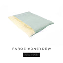 A luxurious Dog Burrow Bag, a sleeping bag style dog bed or snuggle sack style dog bed, with an outer cover in pale sage green woven wool texture upholstery fabric Faroe with a plush, cream faux-fur lining, and a badge with the colour name Honeydew on a white background.