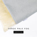A close up detail of the corner of a Charley Chau Burrow Bag Dog Bed with pale grey outer cover in woven wool texture upholstery fabric Faroe and plush cream faux-fur lining with a woven brand label showing the Charley Chau logo on a white backdrop.