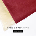 A close up detail of the corner of a Charley Chau Burrow Bag Dog Bed with deep red outer cover in woven wool texture upholstery fabric Faroe and plush cream faux-fur lining with a woven brand label showing the Charley Chau logo on a white backdrop.