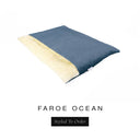 A luxurious Dog Burrow Bag, a sleeping bag style dog bed or snuggle sack style dog bed, with an outer cover in deep teal blue woven wool texture upholstery fabric Faroe with a plush, cream faux-fur lining, and a badge with the colour name Ocean on a white background.