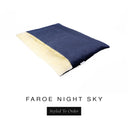 A luxurious Dog Burrow Bag, a sleeping bag style dog bed or snuggle sack style dog bed, with an outer cover in dark navy blue woven wool texture upholstery fabric Faroe with a plush, cream faux-fur lining, and a badge with the colour name Night Sky on a white background.