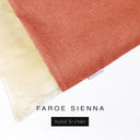 A close up detail of the corner of a Charley Chau Burrow Bag Dog Bed with coral orange outer cover in woven wool texture upholstery fabric Faroe and plush cream faux-fur lining with a woven brand label showing the Charley Chau logo on a white backdrop.