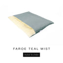 A luxurious Dog Burrow Bag, a sleeping bag style dog bed or snuggle sack style dog bed, with an outer cover in soft teal grey woven wool texture upholstery fabric Faroe with a plush, cream faux-fur lining, and a badge with the colour name Teal Mist on a white background.