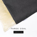 A close up detail of the corner of a Charley Chau Burrow Bag Dog Bed with charcoal black outer cover in woven wool texture upholstery fabric Faroe and plush cream faux-fur lining with a woven brand label showing the Charley Chau logo on a white backdrop.