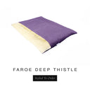 A luxurious Dog Burrow Bag, a sleeping bag style dog bed or snuggle sack style dog bed, with an outer cover in dusty purple woven wool texture upholstery fabric Faroe with a plush, cream faux-fur lining, and a badge with the colour name Deep Thistle on a white background.