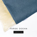 A close up detail of the corner of a Charley Chau Burrow Bag Dog Bed with deep teal blue outer cover in woven wool texture upholstery fabric Faroe and plush cream faux-fur lining with a woven brand label showing the Charley Chau logo on a white backdrop.